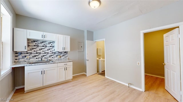 kitchen featuring light wood-type flooring, tasteful backsplash, light stone counters, sink, and white cabinetry