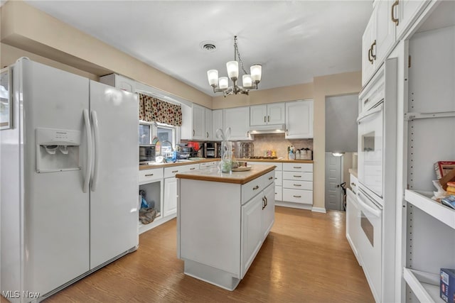 kitchen featuring white appliances, hanging light fixtures, a kitchen island, white cabinetry, and a chandelier