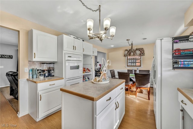 kitchen featuring a center island, a notable chandelier, white appliances, decorative light fixtures, and white cabinets