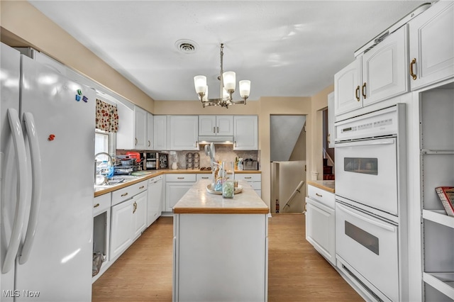 kitchen featuring white appliances, a kitchen island, pendant lighting, a notable chandelier, and white cabinetry