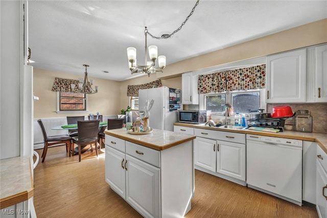 kitchen featuring white appliances, sink, hanging light fixtures, a notable chandelier, and white cabinetry