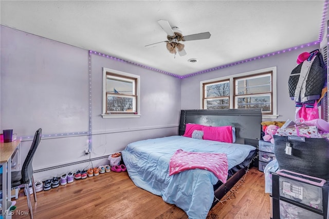 bedroom with wood-type flooring, ceiling fan, and a baseboard heating unit