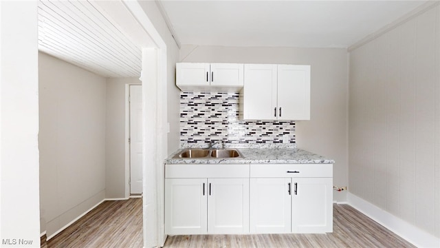 kitchen featuring sink, white cabinetry, light stone countertops, light hardwood / wood-style floors, and backsplash