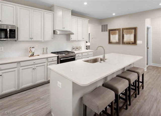 kitchen with light wood-type flooring, stainless steel appliances, a kitchen island with sink, sink, and white cabinetry