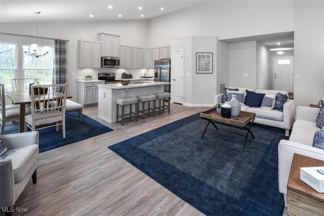 living room with high vaulted ceiling, sink, light hardwood / wood-style floors, and a notable chandelier