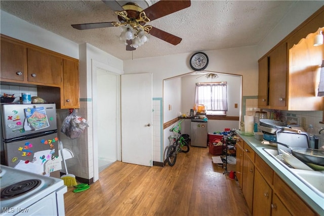 kitchen with white electric stove, stainless steel fridge, a textured ceiling, decorative backsplash, and light wood-type flooring