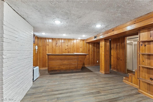 bar featuring wooden walls, dark hardwood / wood-style flooring, and a textured ceiling