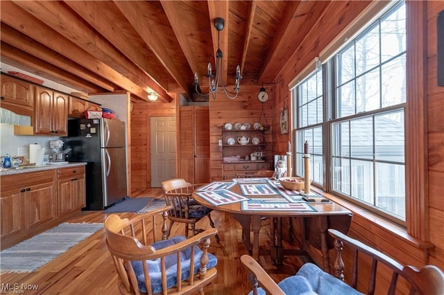 interior space with wood walls, wooden ceiling, light hardwood / wood-style flooring, stainless steel fridge, and beamed ceiling