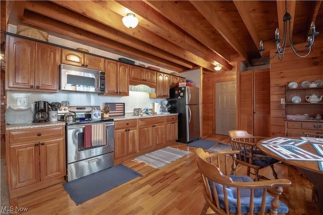 kitchen featuring appliances with stainless steel finishes, light hardwood / wood-style flooring, light stone counters, and wood walls