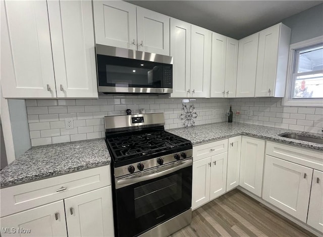 kitchen featuring white cabinetry, light stone countertops, tasteful backsplash, appliances with stainless steel finishes, and hardwood / wood-style flooring