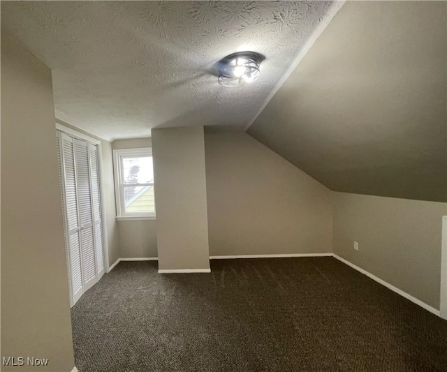 additional living space with a textured ceiling, dark carpet, and vaulted ceiling