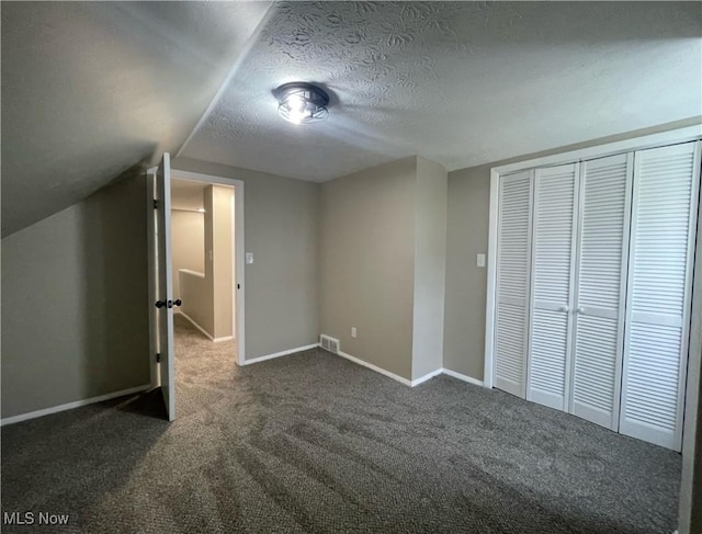 unfurnished bedroom featuring lofted ceiling, a closet, a textured ceiling, and dark colored carpet