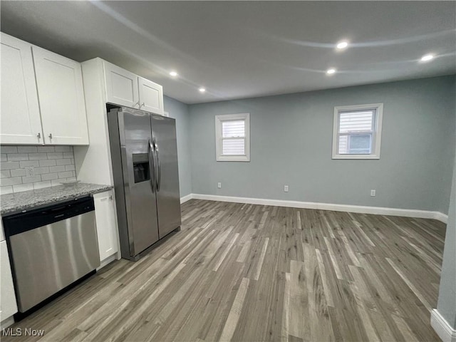 kitchen with white cabinetry, tasteful backsplash, light stone counters, appliances with stainless steel finishes, and light wood-type flooring