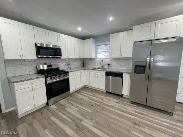 kitchen with light stone counters, light wood-type flooring, white cabinetry, and stainless steel appliances