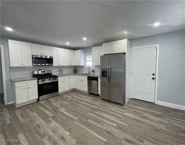 kitchen with appliances with stainless steel finishes, light hardwood / wood-style flooring, white cabinetry, and sink