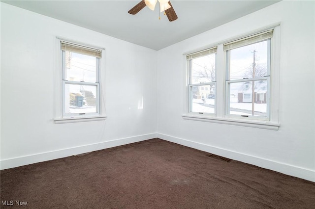 empty room featuring ceiling fan, plenty of natural light, and dark colored carpet