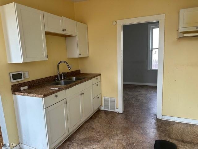 kitchen featuring a sink, visible vents, dark countertops, and white cabinets