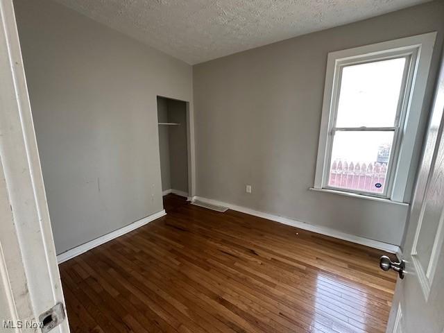 unfurnished bedroom with hardwood / wood-style flooring, baseboards, a closet, and a textured ceiling