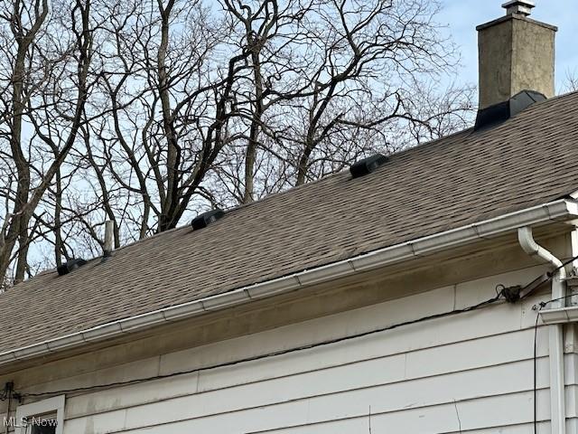 exterior details with a downspout, a chimney, gutters, and roof with shingles