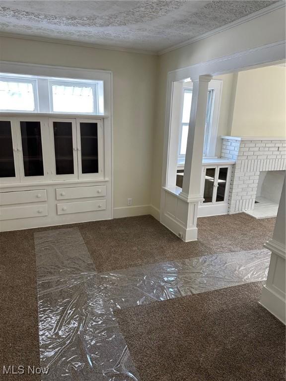 unfurnished living room featuring a textured ceiling, ornate columns, and crown molding