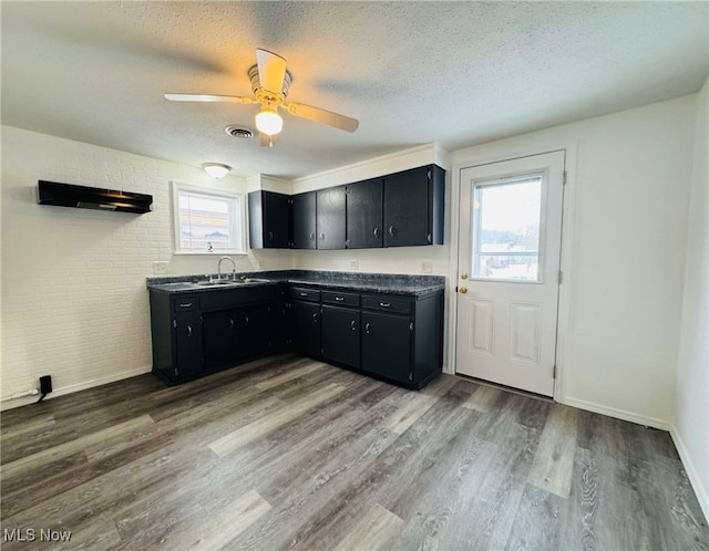 kitchen featuring ceiling fan, sink, dark wood-type flooring, brick wall, and a textured ceiling