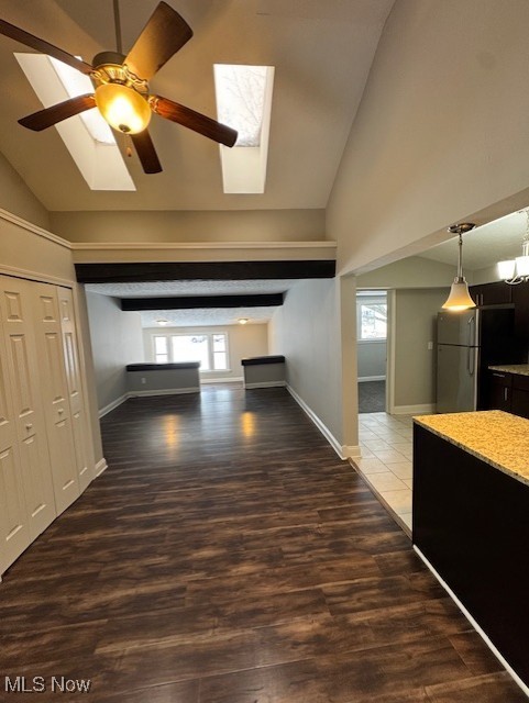 unfurnished living room featuring a healthy amount of sunlight, lofted ceiling with skylight, dark wood-type flooring, and ceiling fan with notable chandelier