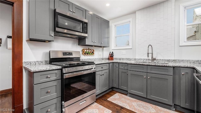 kitchen with gray cabinetry, light stone countertops, sink, and stainless steel appliances