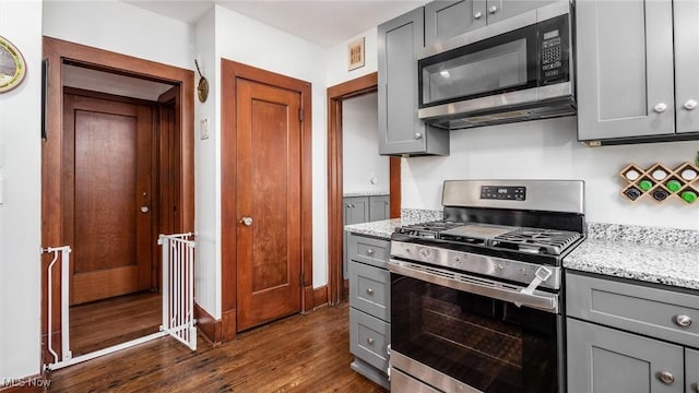 kitchen featuring gray cabinets, light stone counters, dark hardwood / wood-style flooring, and appliances with stainless steel finishes