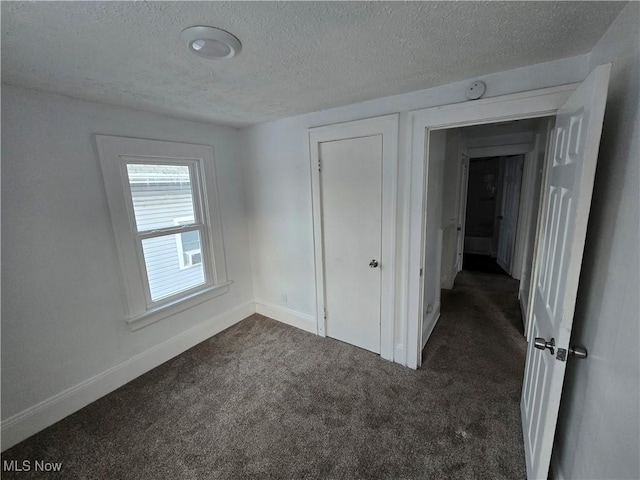 spare room featuring dark carpet and a textured ceiling