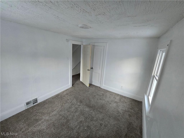 spare room with dark colored carpet and a textured ceiling