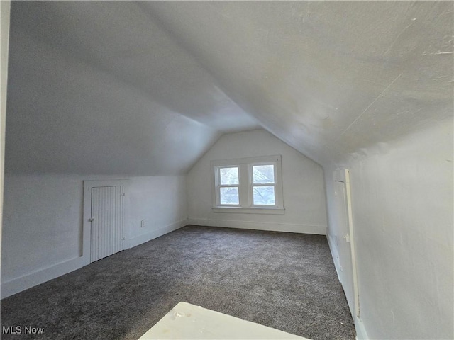 additional living space featuring vaulted ceiling and dark colored carpet