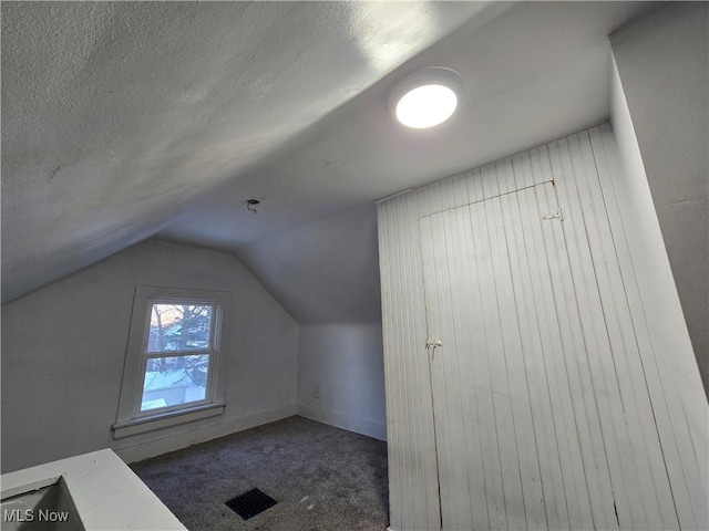 additional living space featuring a textured ceiling, dark carpet, and lofted ceiling