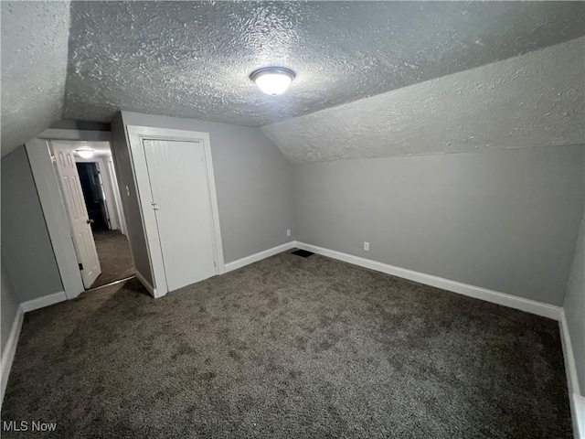 bonus room featuring lofted ceiling, baseboards, dark colored carpet, and a textured ceiling