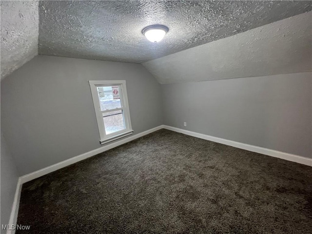 additional living space with dark colored carpet, baseboards, a textured ceiling, and vaulted ceiling