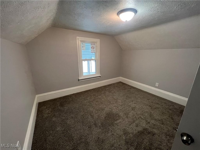 additional living space featuring vaulted ceiling, baseboards, dark carpet, and a textured ceiling