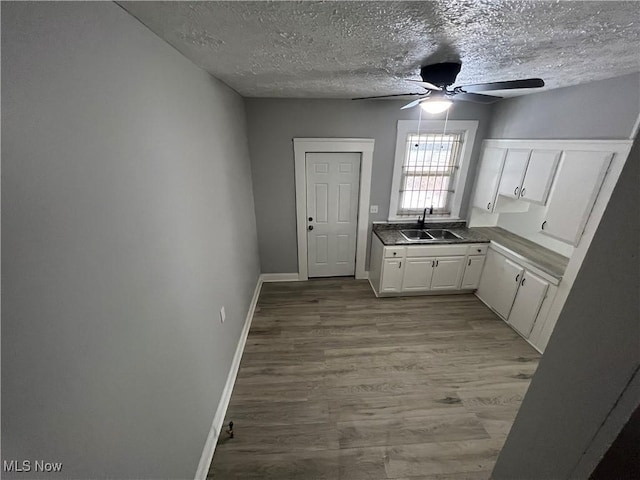 kitchen featuring baseboards, light wood finished floors, a sink, a textured ceiling, and white cabinetry