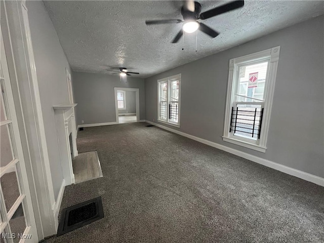 unfurnished living room featuring dark colored carpet, visible vents, baseboards, and a textured ceiling