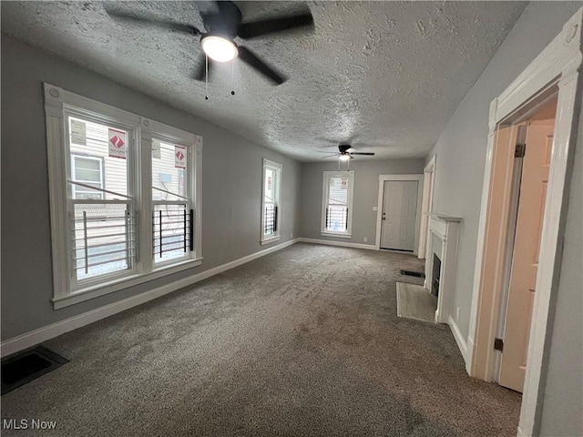 unfurnished living room featuring visible vents, a fireplace with flush hearth, a textured ceiling, carpet flooring, and baseboards