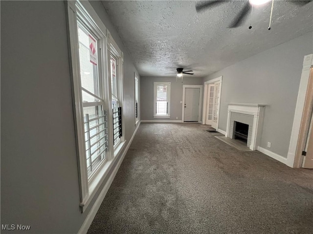 unfurnished living room with a ceiling fan, carpet, baseboards, a fireplace with flush hearth, and a textured ceiling