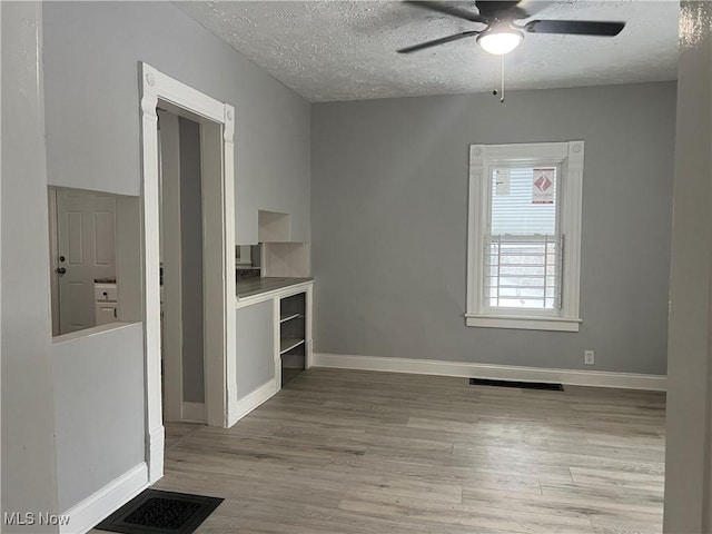 spare room featuring a ceiling fan, baseboards, wood finished floors, visible vents, and a textured ceiling