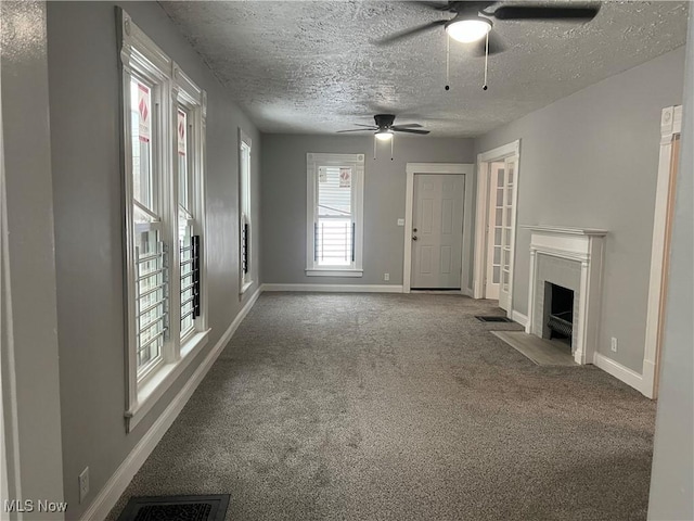 unfurnished living room featuring visible vents, baseboards, a fireplace with flush hearth, a textured ceiling, and carpet flooring