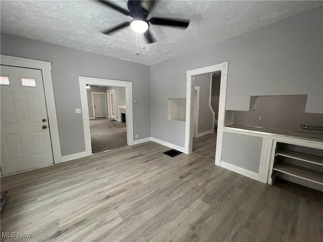 unfurnished living room with ceiling fan, baseboards, a textured ceiling, and wood finished floors