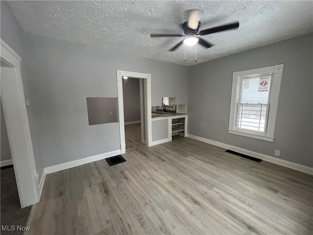 interior space with visible vents, a textured ceiling, baseboards, and wood finished floors