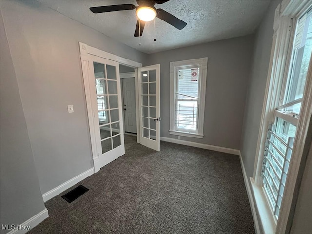 unfurnished room featuring visible vents, a textured ceiling, dark carpet, and french doors