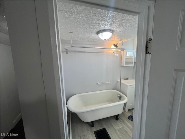 full bathroom featuring visible vents, a freestanding bath, vanity, wood finished floors, and a textured ceiling