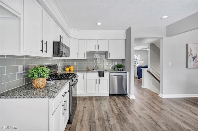 kitchen with sink, dark stone counters, wood-type flooring, white cabinets, and appliances with stainless steel finishes