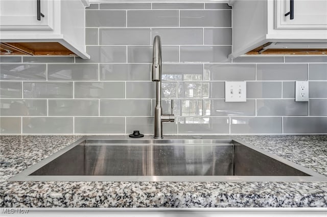 kitchen with backsplash, white cabinetry, sink, and light stone countertops