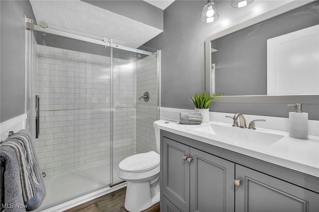 bathroom with hardwood / wood-style floors, vanity, toilet, and a shower with door