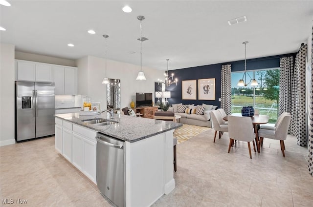 kitchen featuring light stone counters, stainless steel appliances, a kitchen island with sink, sink, and white cabinetry