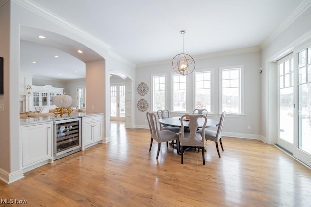 dining room with light wood-type flooring, an inviting chandelier, wine cooler, and crown molding